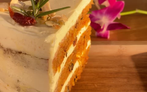 A piece of carrot cake on a table outdoors with a orchid in the background at the cafe with the best tea in Rawai: Poached Breakfast Cafe Rawai, Phuket, Thailand